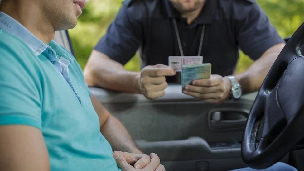 Scena wewnątrz pojazdu, gdzie policjant zabiera prawo jazdy od kierowcy